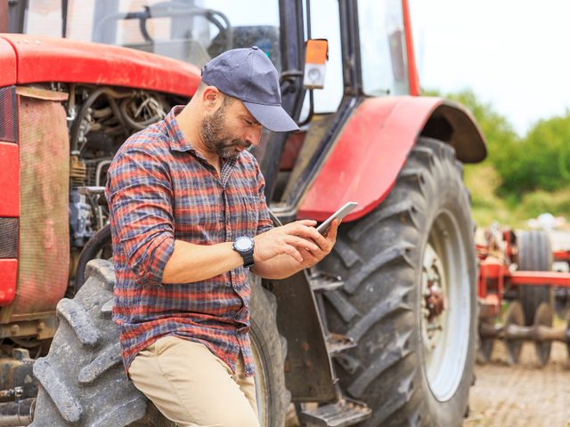 Farmer leaning on tractor texting Feed Bucket for Text Support Service, Simpsonville, KY